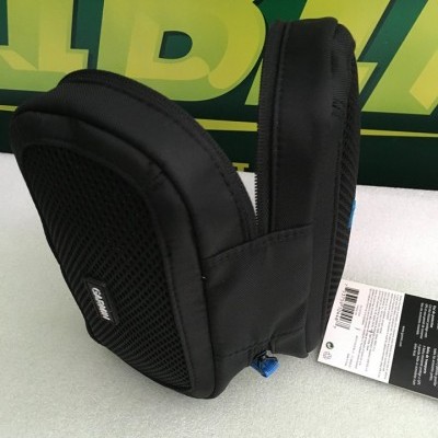 Bolsa pequena preta com etiqueta OZUKO colocada sobre superfície branca com fundo verde.