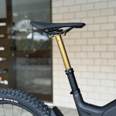 Selim de bicicleta de montanha com suspensão dourada ajustável e pneu tratorado num fundo de parede de tijolos brancos