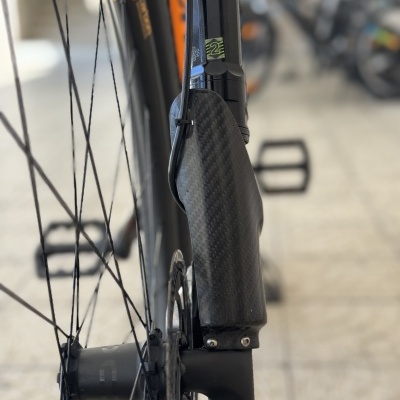 Roda de bicicleta preta com guarda-lamas em fibra de carbono e quadro laranja ao fundo