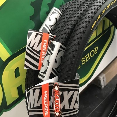 Pneu de bicicleta preto texturizado com etiqueta Maxxis em fundo verde e amarelo de loja