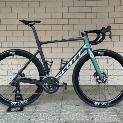 Bicicleta de estrada verde e preta com rodas DT SWISS encostada a parede de azulejos