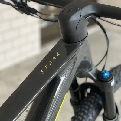 Bicicleta de montanha preta SPARK com guiador e pneus grossos junto a uma parede de azulejos brancos