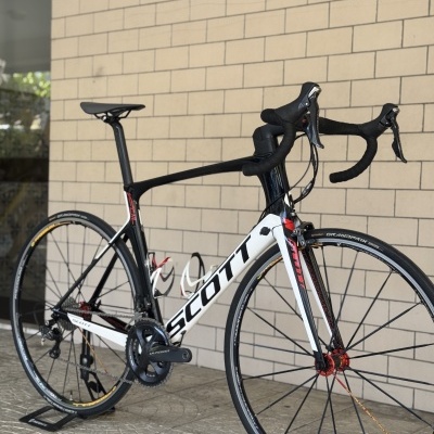 Bicicleta de estrada SCOTT branca e preta encostada numa parede de tijolos