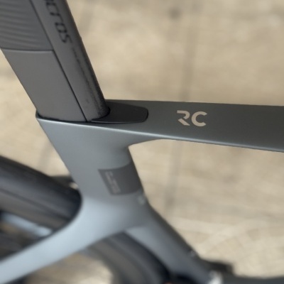 Quadro de bicicleta cinza fosco com logotipo RC e selim Syncros em fundo claro