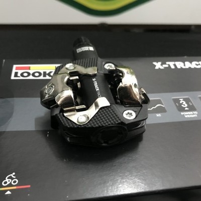 Pedal de bicicleta preto e metálico sobre caixa preta com texto e ícones