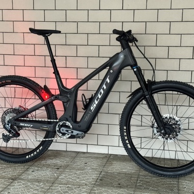 Bicicleta de montanha elétrica preta SCOTT encostada a parede de azulejos brancos.