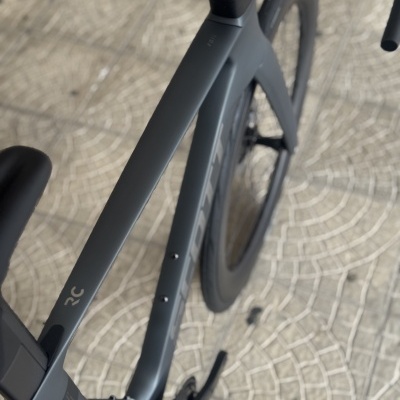 Bicicleta de estrada cinza escuro fosco com rodas e detalhes em preto, vista de cima sobre pavimento de mosaico claro