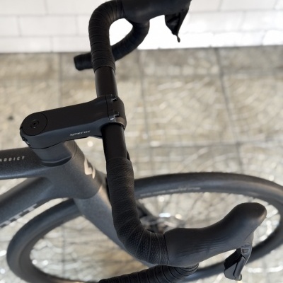 Guidão de bicicleta preta com fita texturizada e manetes integradas.