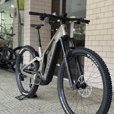 Bicicleta elétrica de montanha SCOTT cinza com pneus Maxxis exposta em interior
