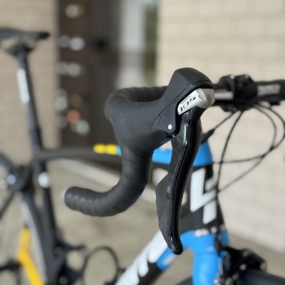 Bicicleta de estrada azul-branca com guiador preto e componente Shimano 105.