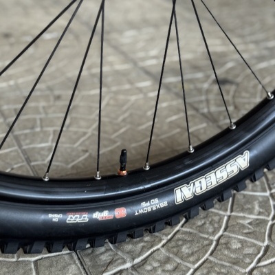 Pneu de bicicleta preto ASSEGAI em detalhamento com aro e raios pretos sobre pavimento cinza