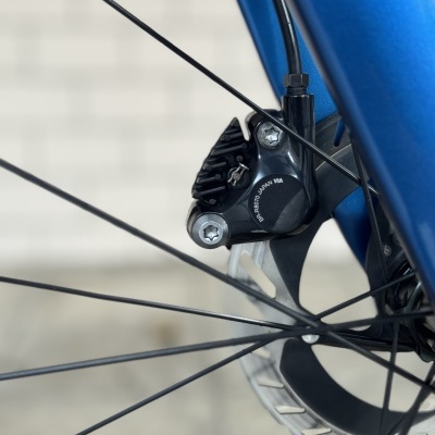 Sistema de travão de disco preto em bicicleta azul com rotor metálico e texto impresso