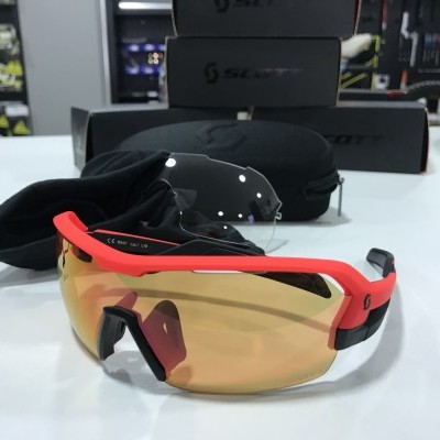 Óculos desportivos vermelhos e pretos com lentes amarelas, ao lado de capas e caixas SILENT