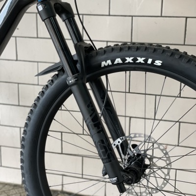 Pneu Maxxis e suspensão dianteira de bicicleta em fundo de azulejos brancos.