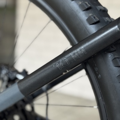 Zoom num pneu de bicicleta preto com piso espesso e texto 140 MM numa estrutura metálica preta.