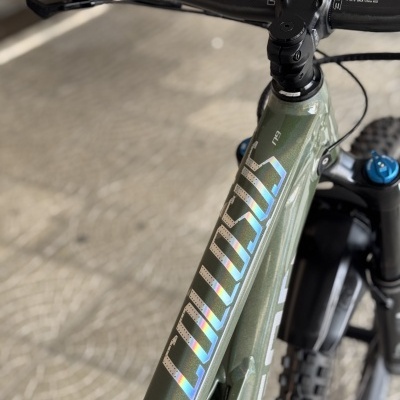 Bicicleta de montanha verde metálica com letras holográficas COMMENCAL e guiador preto