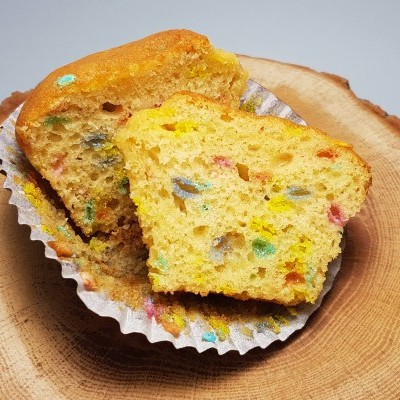Muffin amarelo com pedaços coloridos em forma de papel branca sobre base de madeira