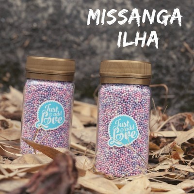 Dois frascos com missangas coloridas em folhas secas com texto MISSANGA ILHA.