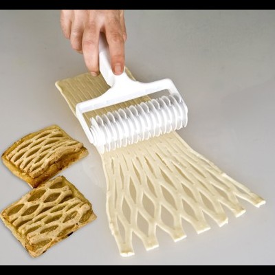 Rolo de corte de massa com padrão geométrico e massa cortada em superfície cinza