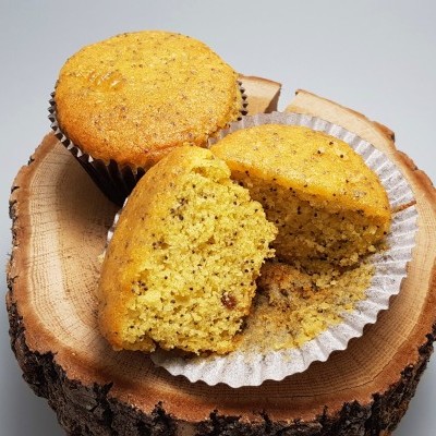 Dois muffins amarelos com sementes em forminhas de papel sobre tronco de madeira
