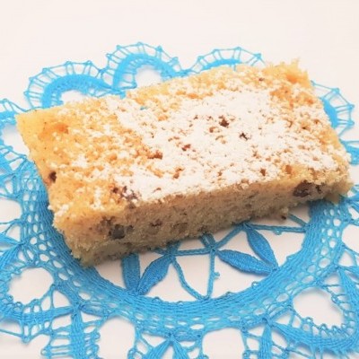 Fatia de bolo com cobertura branca sobre toalha azul rendada