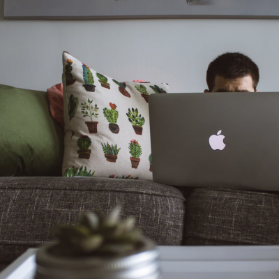 Almofadas decorativas num sofá cinzento com homem usando portátil Apple