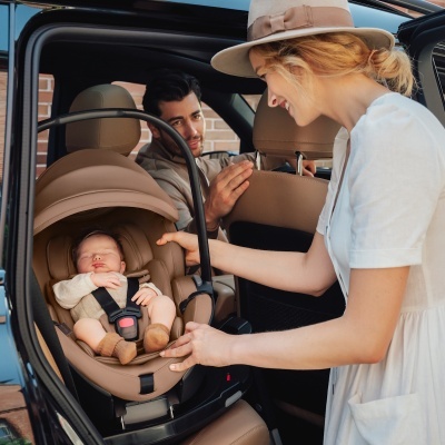 Cadeira de bebé bege no carro com mulher e homem próximos
