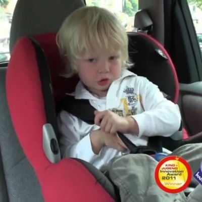 Criança num cadeirão auto vermelho a ajustar o cinto dentro do carro com selos de prémios visíveis