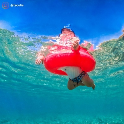 Criança com bóia insuflável vermelha em forma de anel na água clara