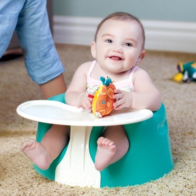 Bebé sentado em cadeira verde com tabuleiro branco segurando brinquedo colorido