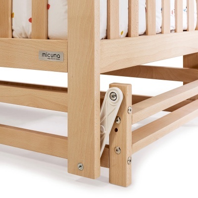 Berço de madeira clara com etiqueta micuna e colchão branco com manchas coloridas