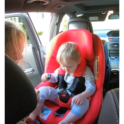 Cadeira auto vermelha com bebé e mulher em carro cinzento.