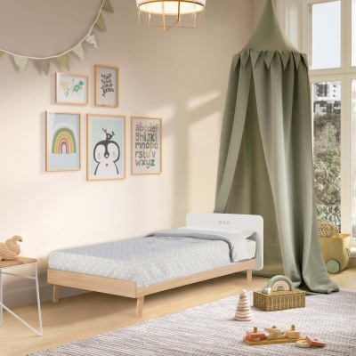 Quarto infantil com cama de madeira clara, tecto de tecido verde, quadros coloridos e brinquedos de madeira