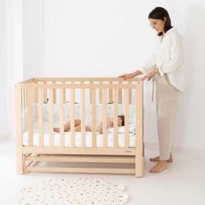 Berço de madeira clara com bebé a dormir e mulher ao lado