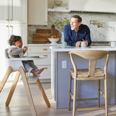 Cadeira alta para bebé com estrutura em madeira clara e assento branco, numa cozinha moderna