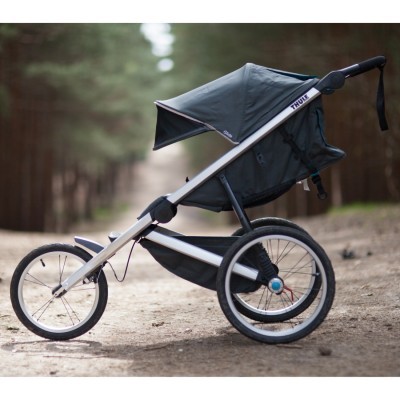 Carrinho desportivo de criança preto com estrutura metálica em caminho de terra na floresta