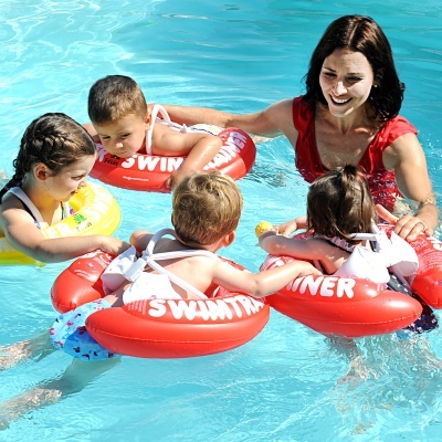 Quatro crianças com boias e uma mulher vestida de vermelho numa piscina