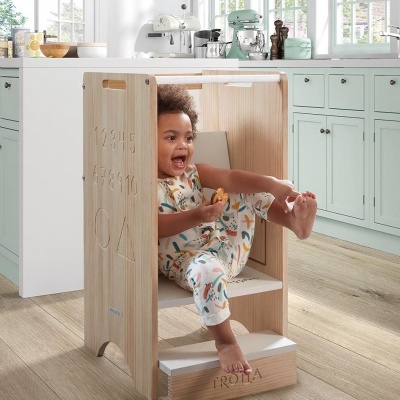 Criança sentada numa cadeira de aprendizagem em madeira clara com números e formas gravados, em cozinha moderna verde-água