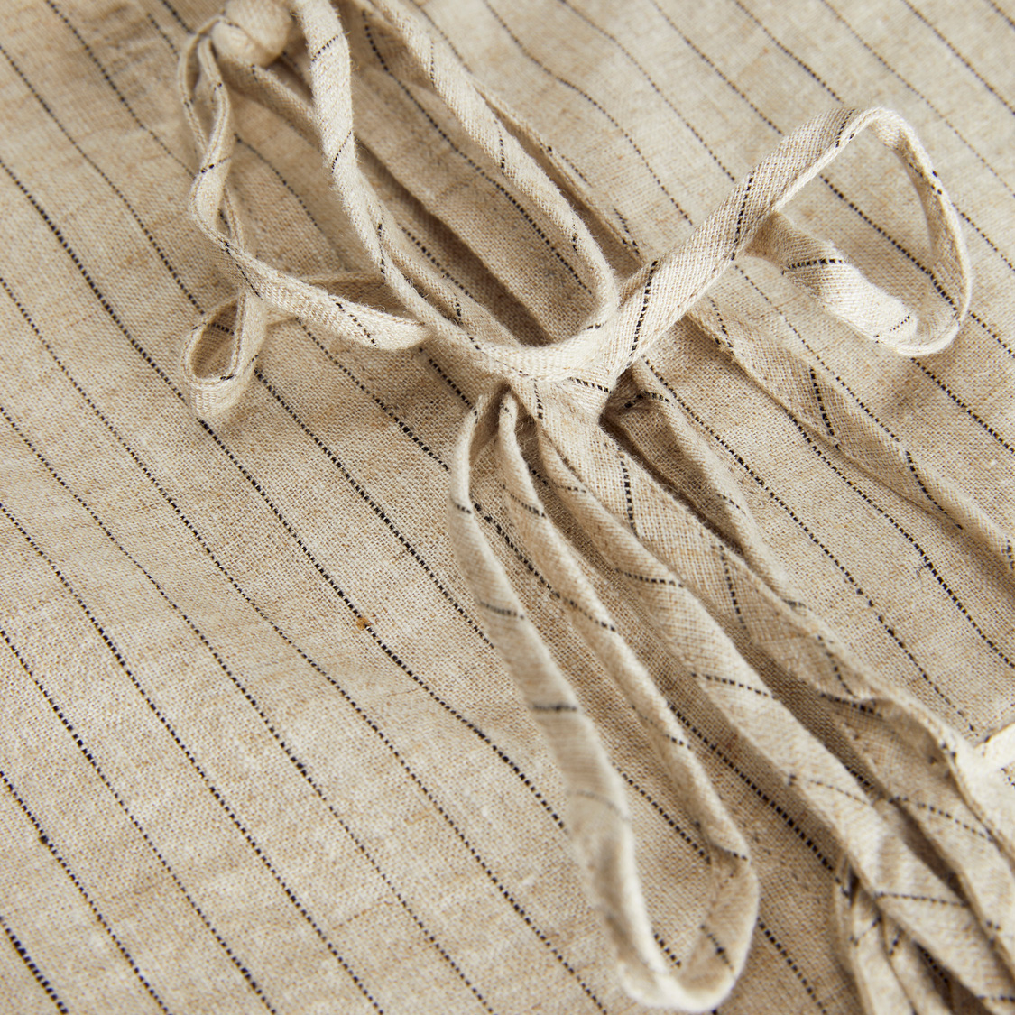 Tecido bege com riscas pretas e cordões para amarrar