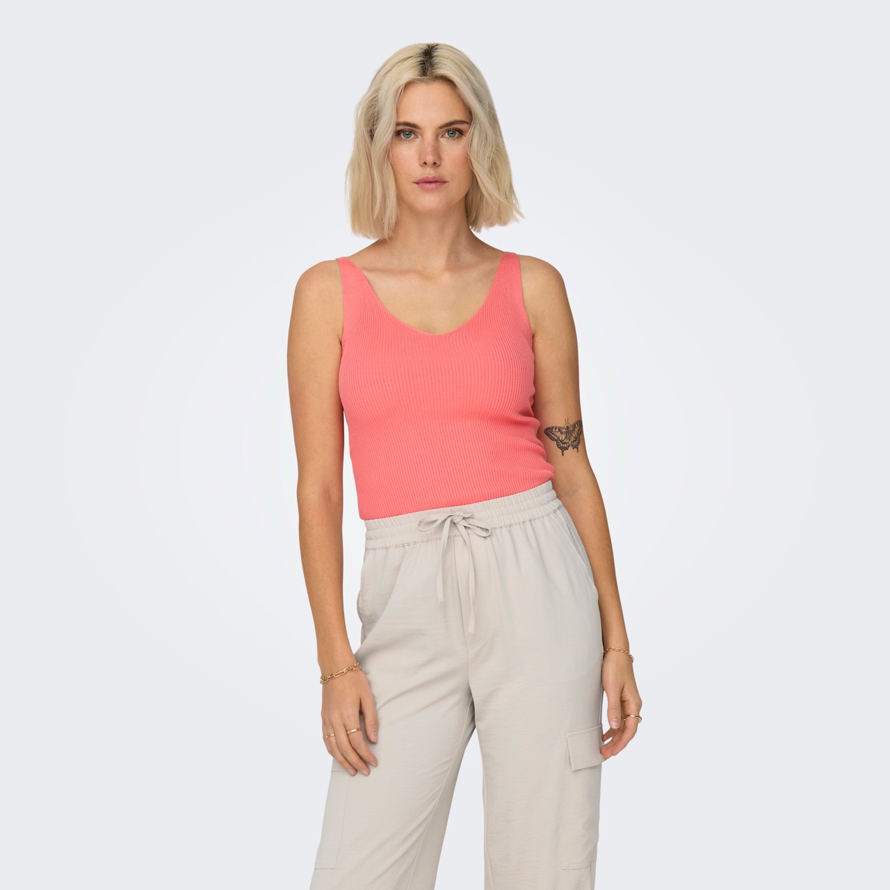 Mulher com top cor de coral e calças largas bege