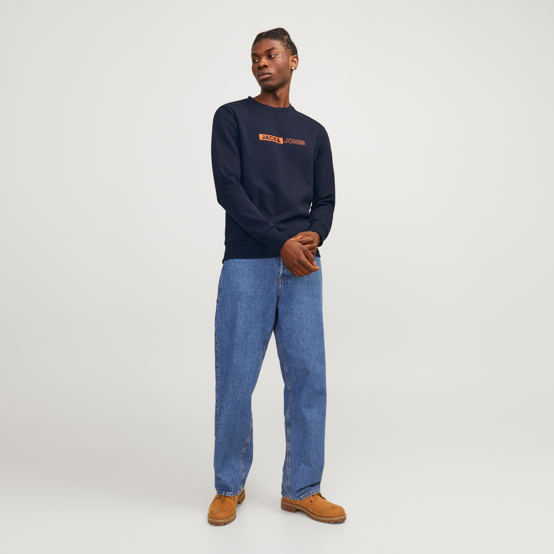 Homem com camisola azul escura JACK & JONES, jeans azuis largos e botas castanhas