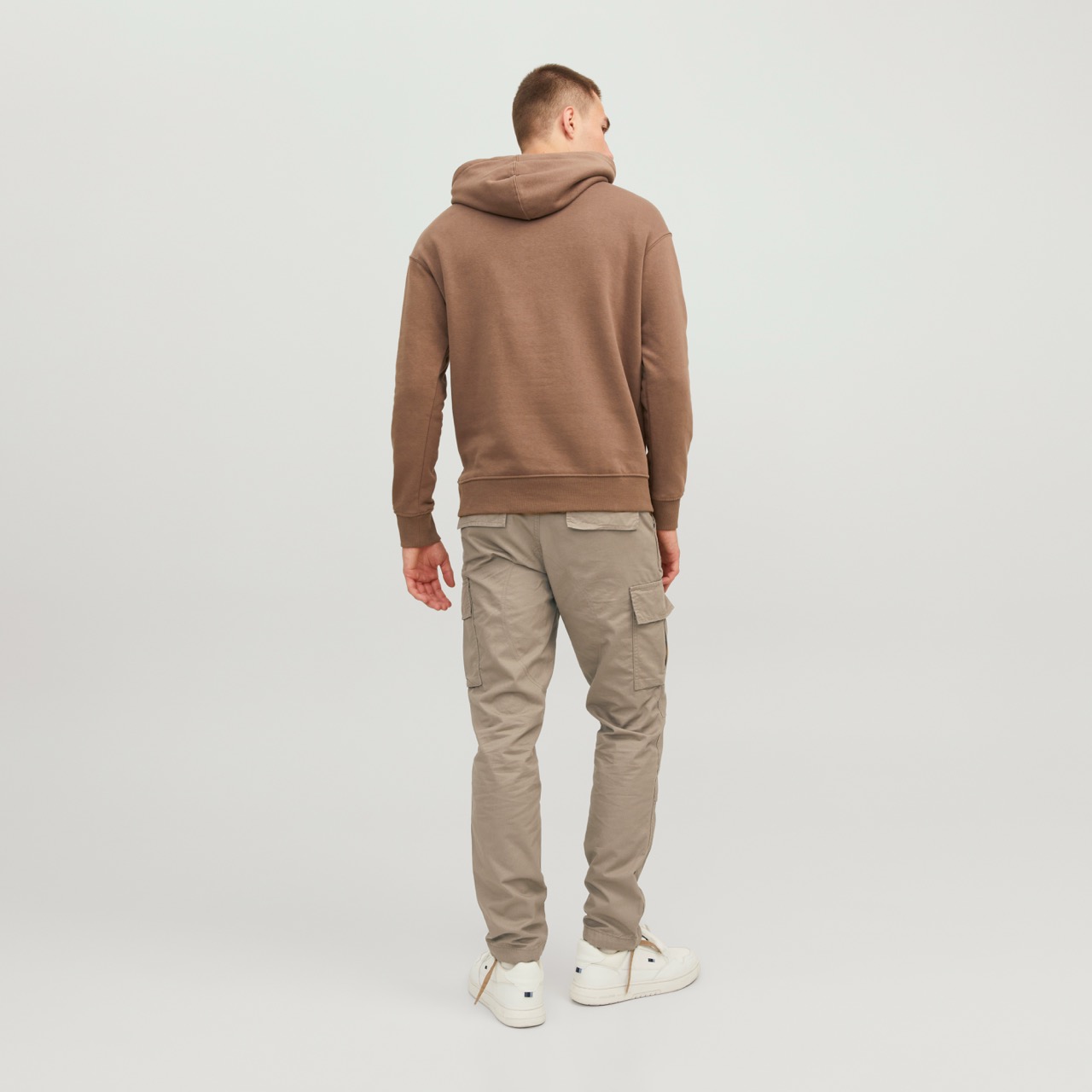 Pessoa de costas com hoodie castanho, calças cargo bege e sapatilhas brancas