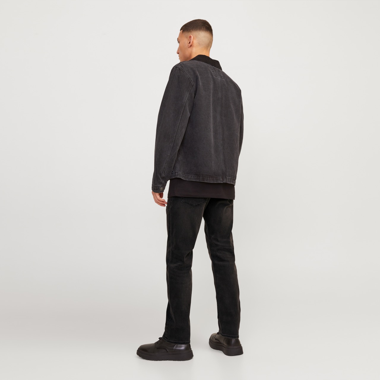 Homem vestido todo de preto visto de costas em fundo branco