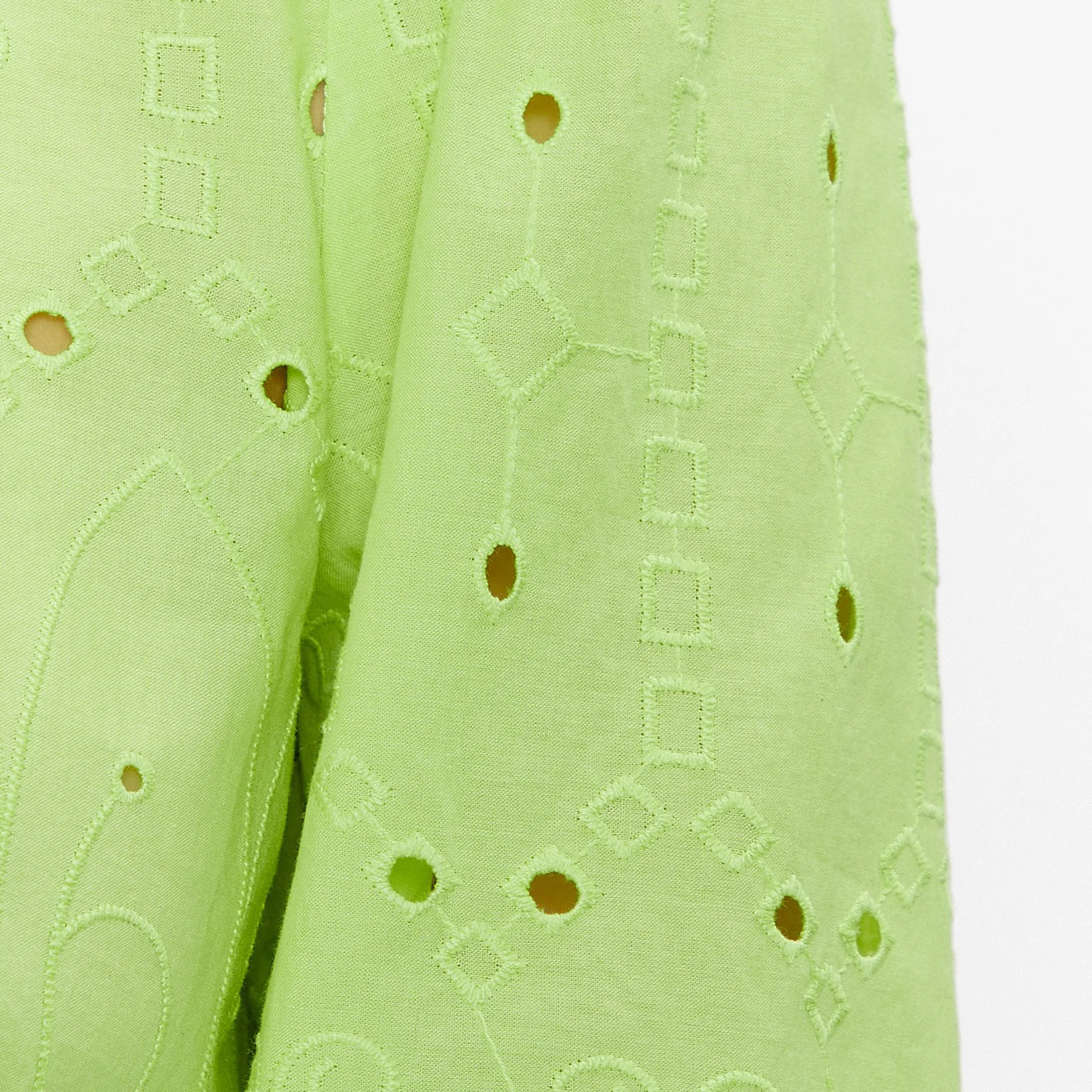 Têxtil verde claro com bordados geométricos e buracos circulares