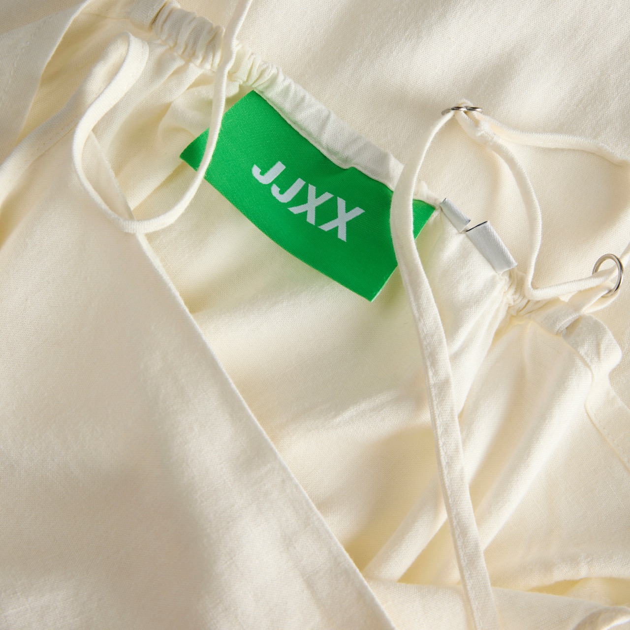 Pormenor de roupa creme com etiqueta verde JJXX e cordões