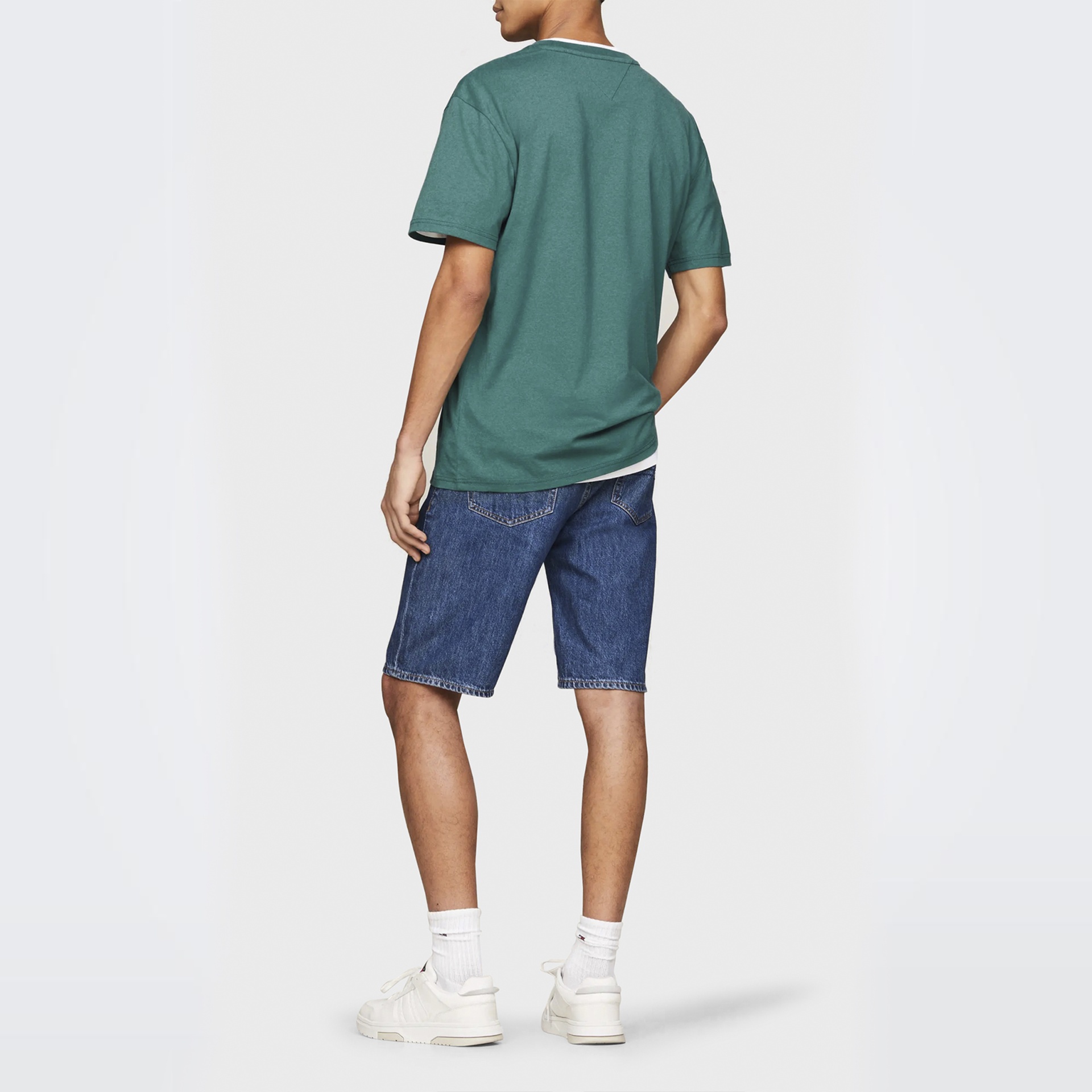 Homem de costas com camisola verde e calções de ganga azul