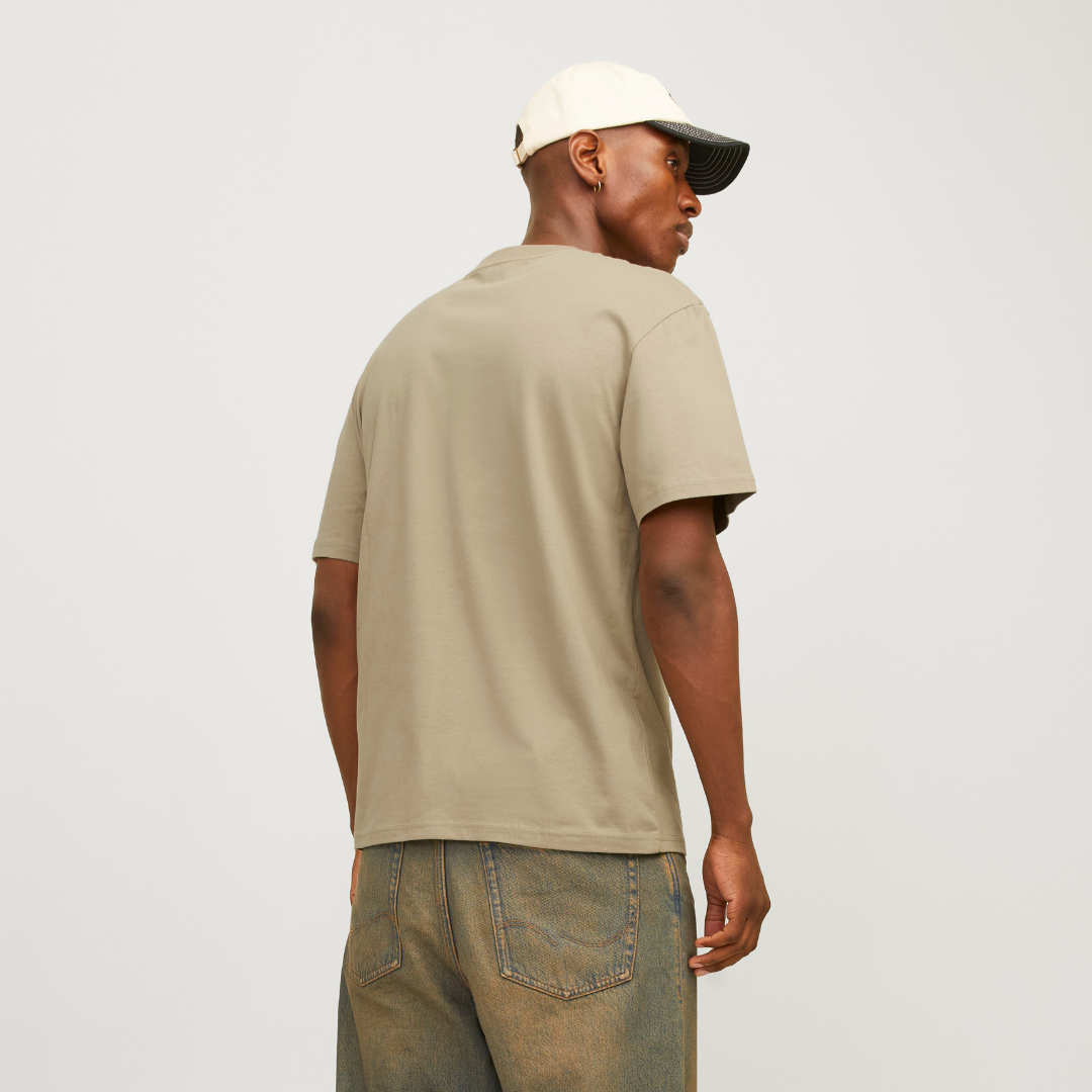 Modelo de costas com camiseta bege, calças jeans azul-esverdeado e boné branco e preto.