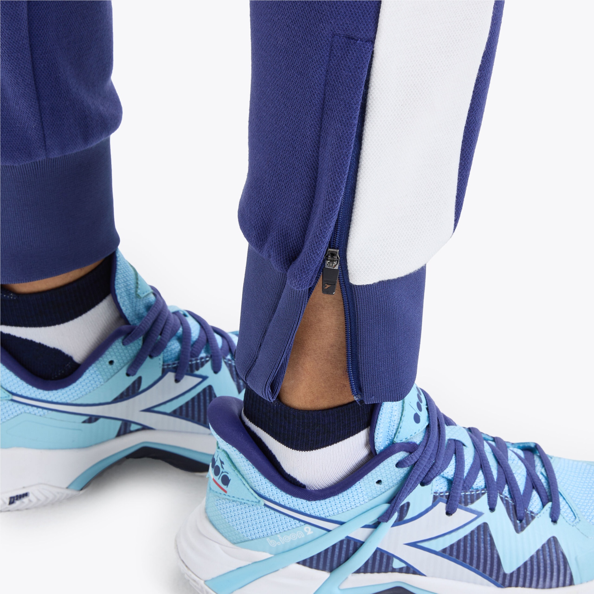 Ténis azuis claros com detalhes em azul escuro e atacadores roxos, usados com calças azuis e meias pretas e brancas