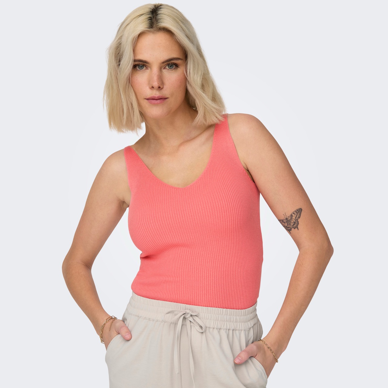 Mulher com top cor de coral e calças cinza claro