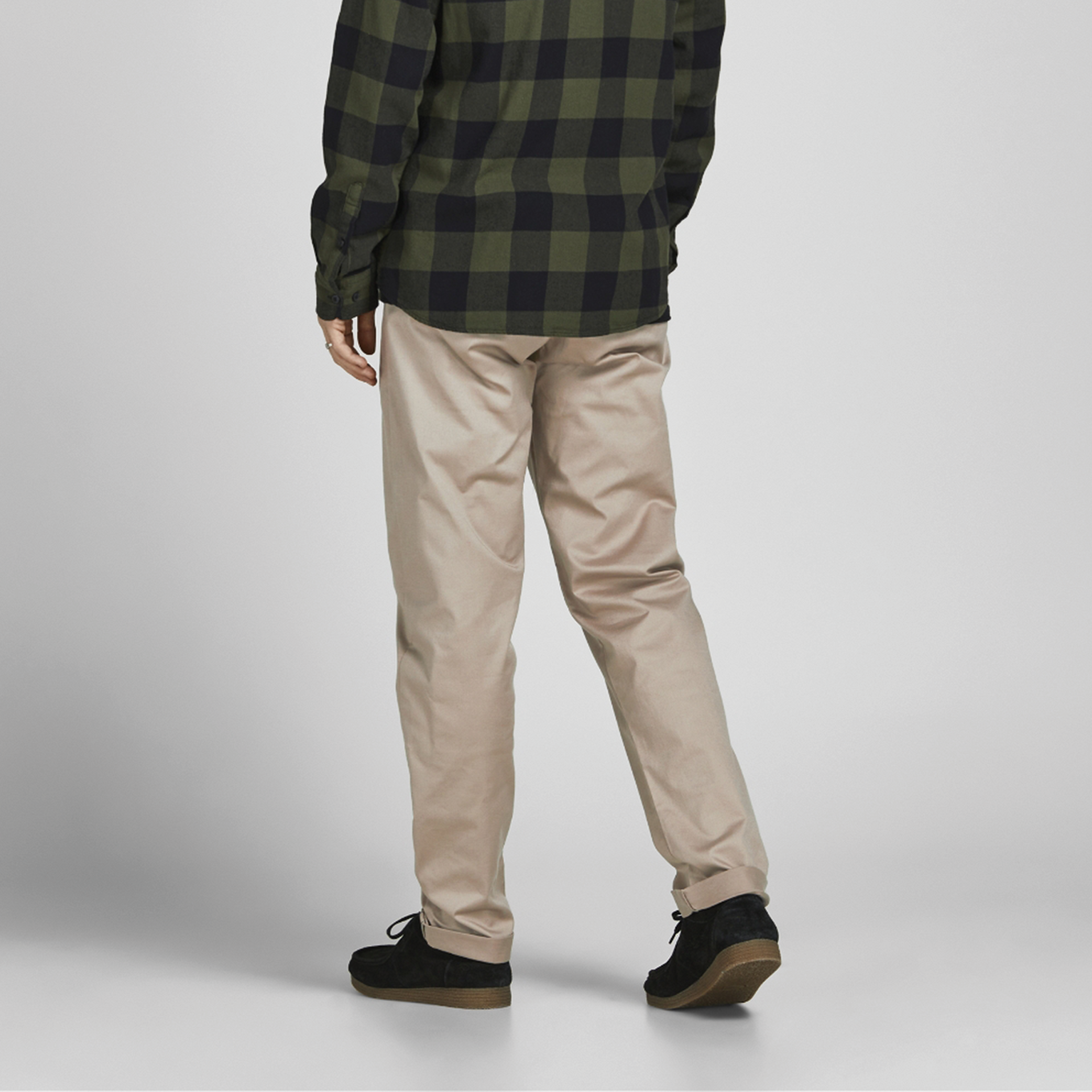 Pessoa com calças bege e camisa xadrez verde e preta, sapatos pretos em fundo branco